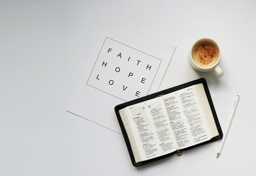 flat lay photography of mug beside opened book and white printer paper