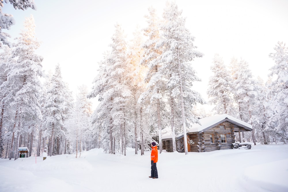 man in orange top standing near trees on snow-covered field