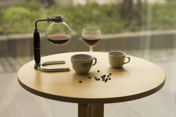A sleek stainless steel coffee jug placed on a wooden table with coffee beans scattered around.