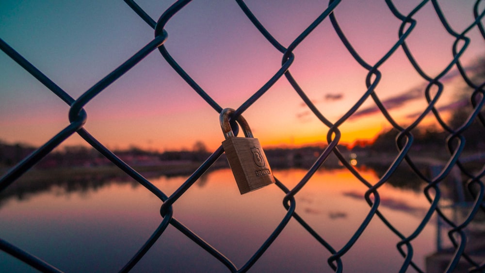 closeup photo of gray padlock locked on gray mesh fence