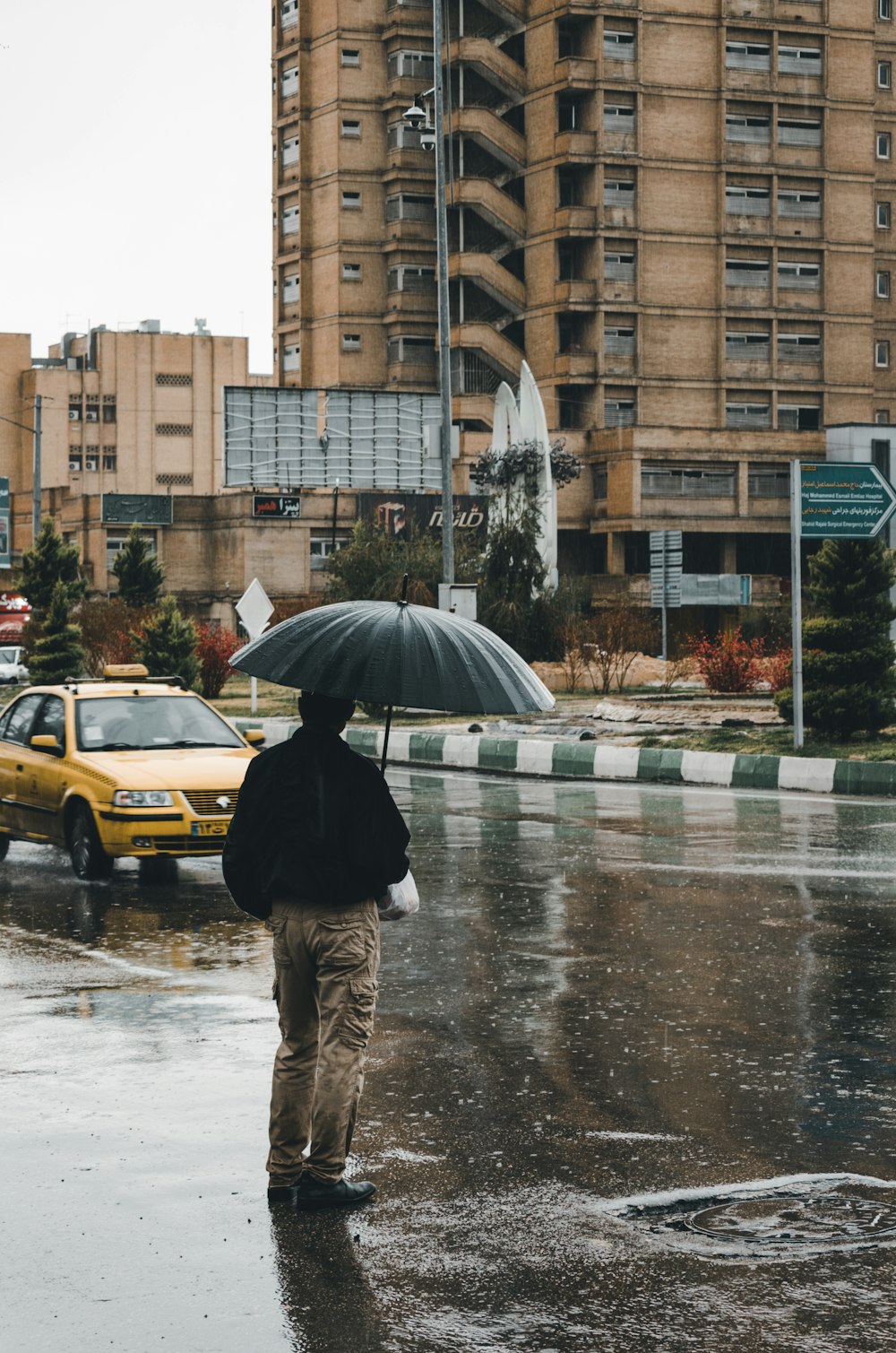 Mann mit Regenschirm, der in der Nähe von Fahrzeugen und Gebäuden steht
