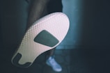 A close-up image of a shoe sole showing a textured pattern with a small logo in the center. The background is slightly blurred, and a person wearing the shoe is partially visible.