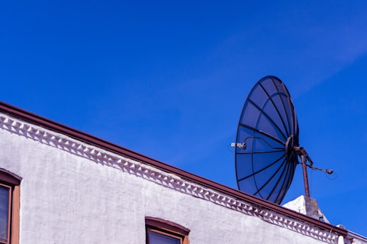 Technician installing a satellite dish on a rooftop with clear sky background.