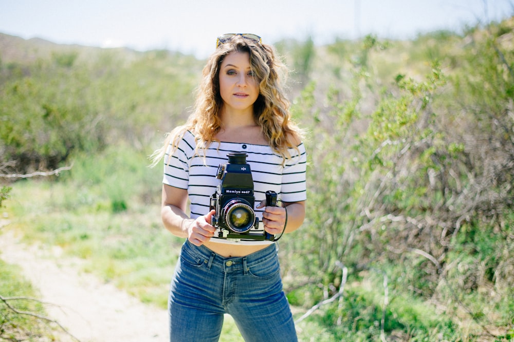 woman holding camera standing near green tall grass during daytime