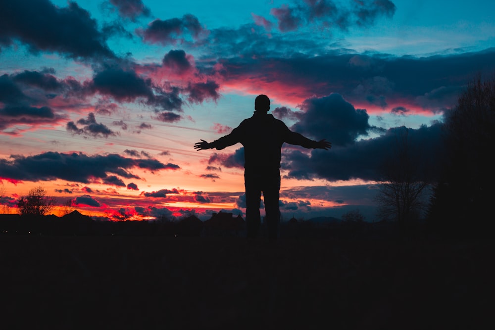 une personne debout dans un champ au coucher du soleil