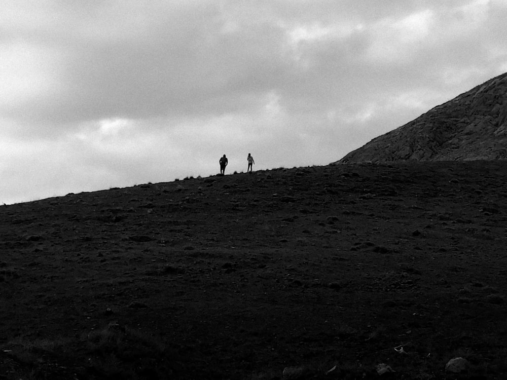 silhouette of 2 people standing on hill under cloudy sky during daytime