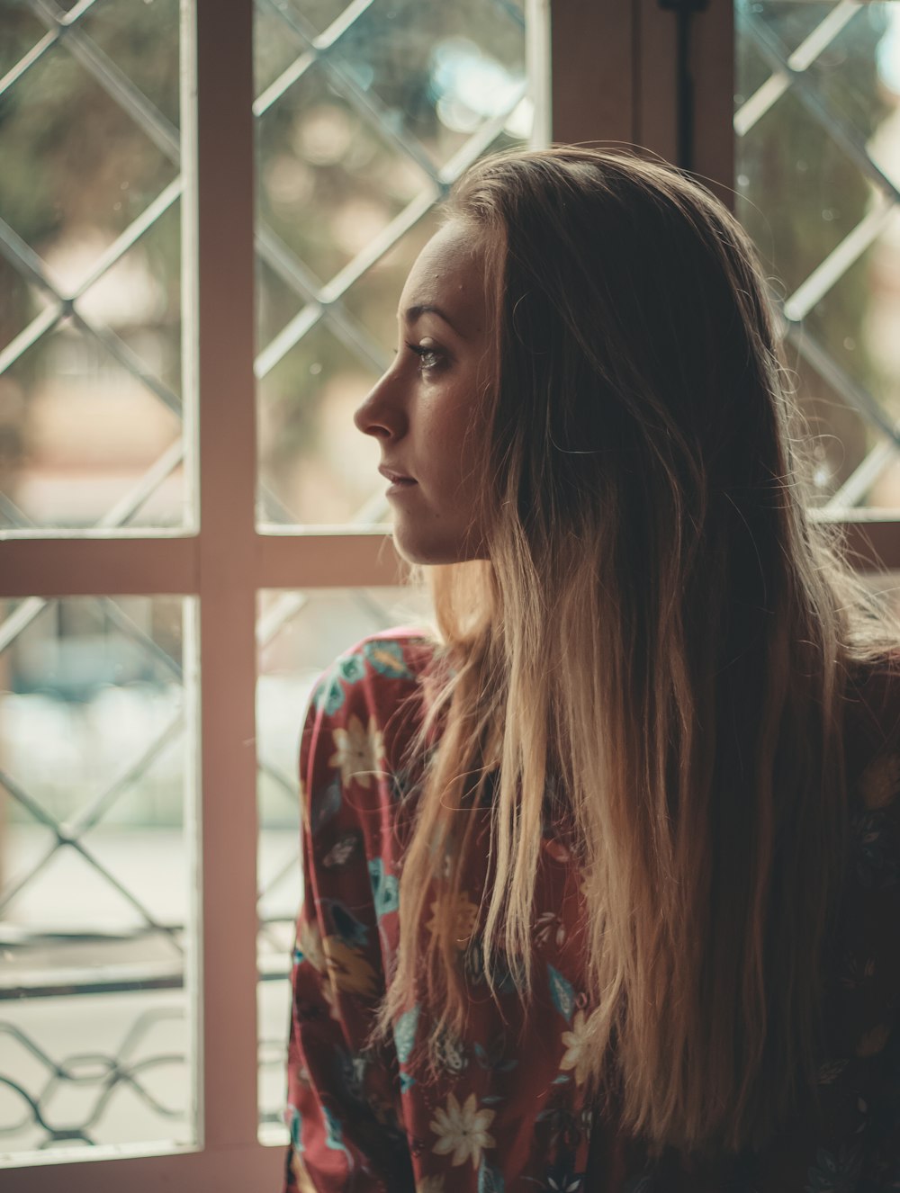 woman wearing red, blue, and yellow floral top besides window