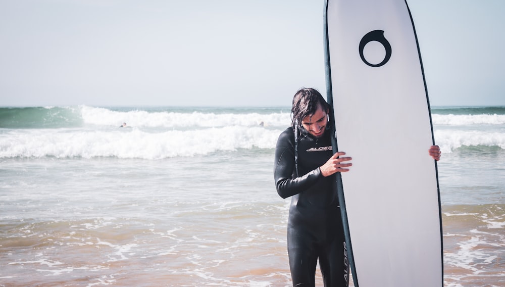 man holding white surfboard standing on shoreline