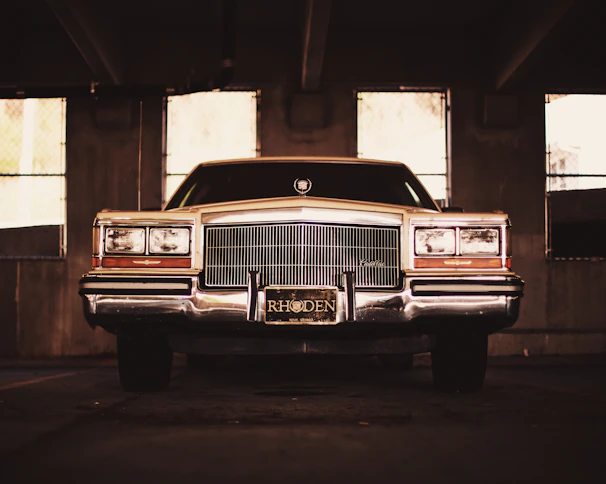 A vintage rat rod car parked in a rustic garage with neon 'Online Garage' sign above.