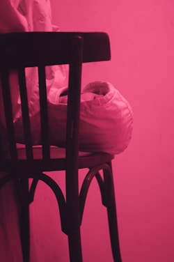 A delicate arrangement of soft pink and beige fabrics draped over a vintage wooden chair, bathed in warm natural light.