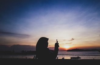 A sunset over the ocean with a silhouette of a person holding a tablet, symbolizing digital connection.