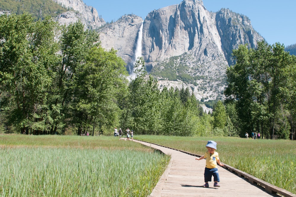 boy in yellow shirt walking on wooden pathway