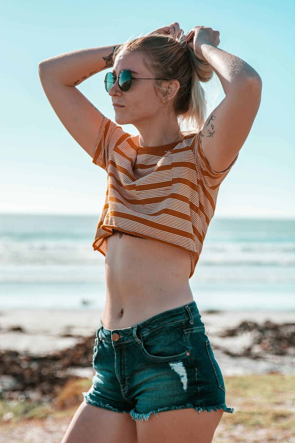 woman wearing brown and yellow striped crop top shirt and distressed blue denim short shorts