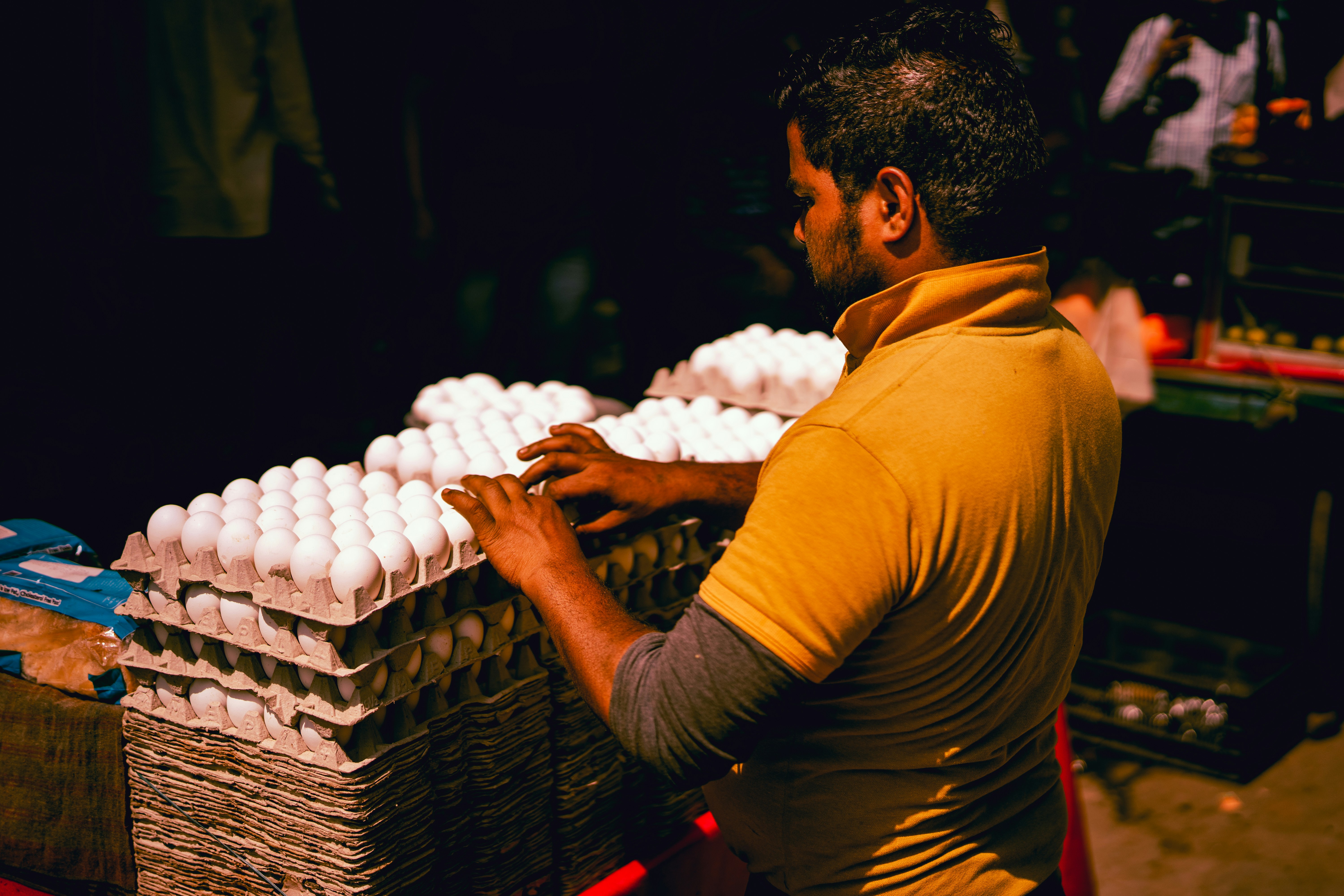 man in brown collared shirt arranging eggs on trays