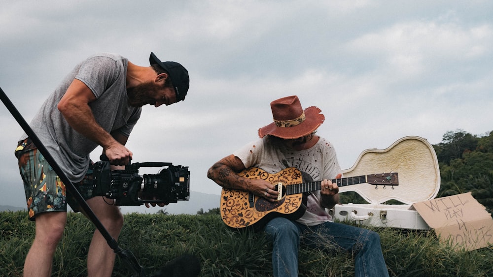 man playing guitar beside man holding video camera during daytime