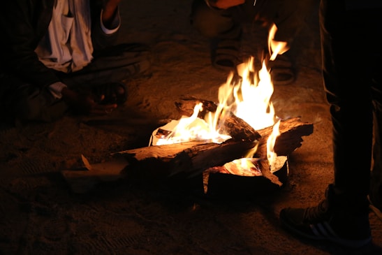 A warm desert campfire surrounded by people playing drums under a glowing full moon.
