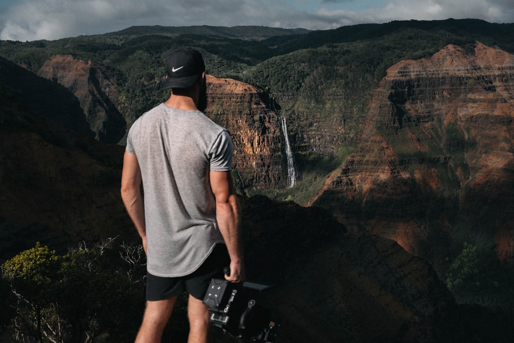 man in gray shirt and black Nike cap standing near canyon