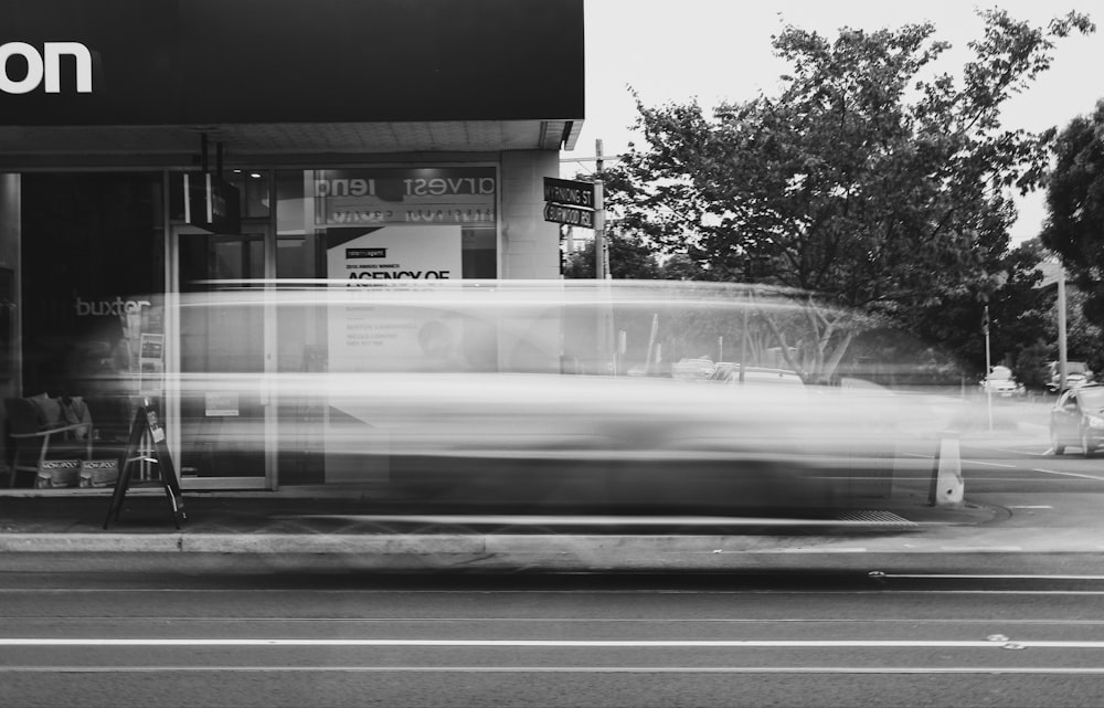 a black and white photo of a car passing by a store
