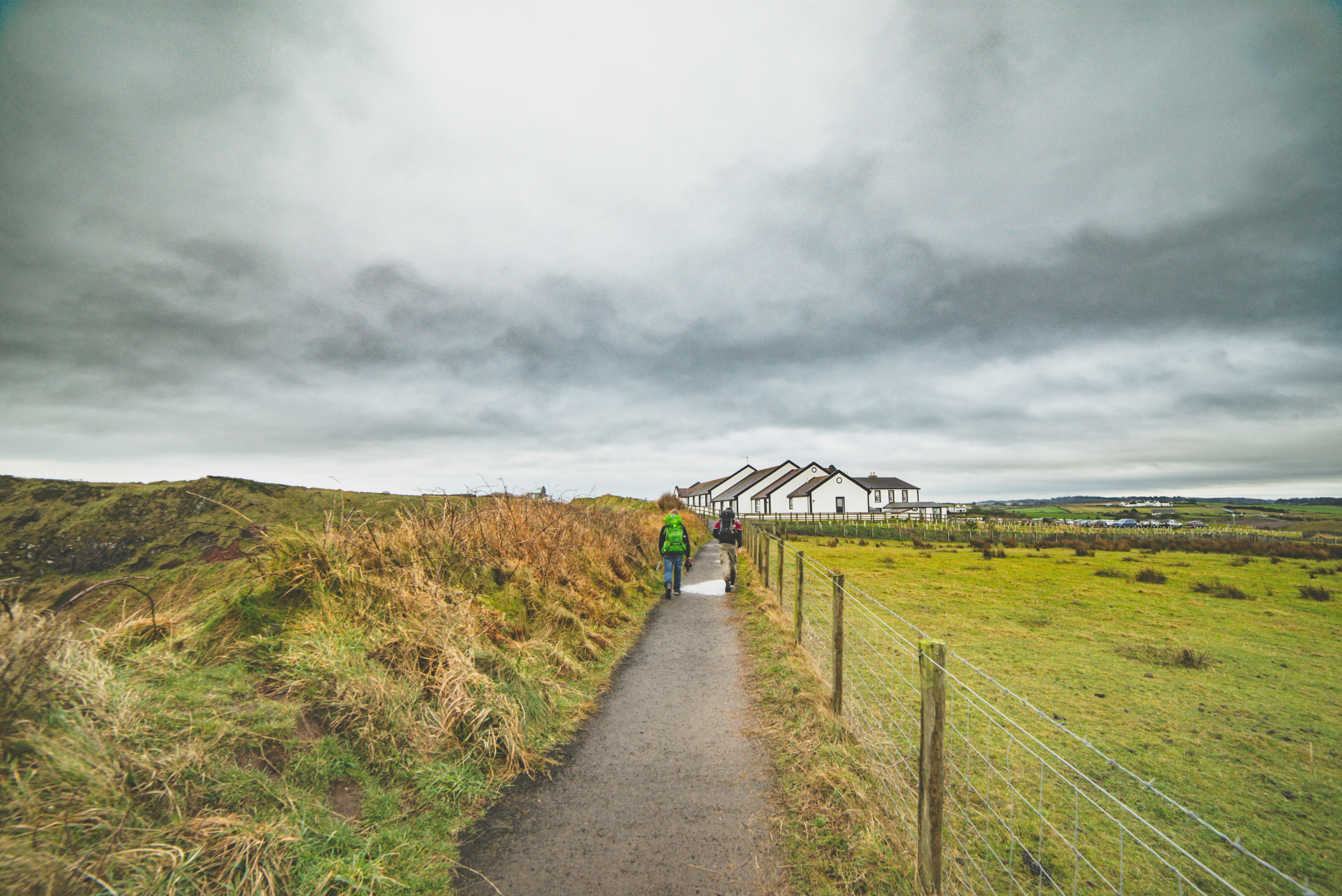 two people walking on roadway between field during daytime