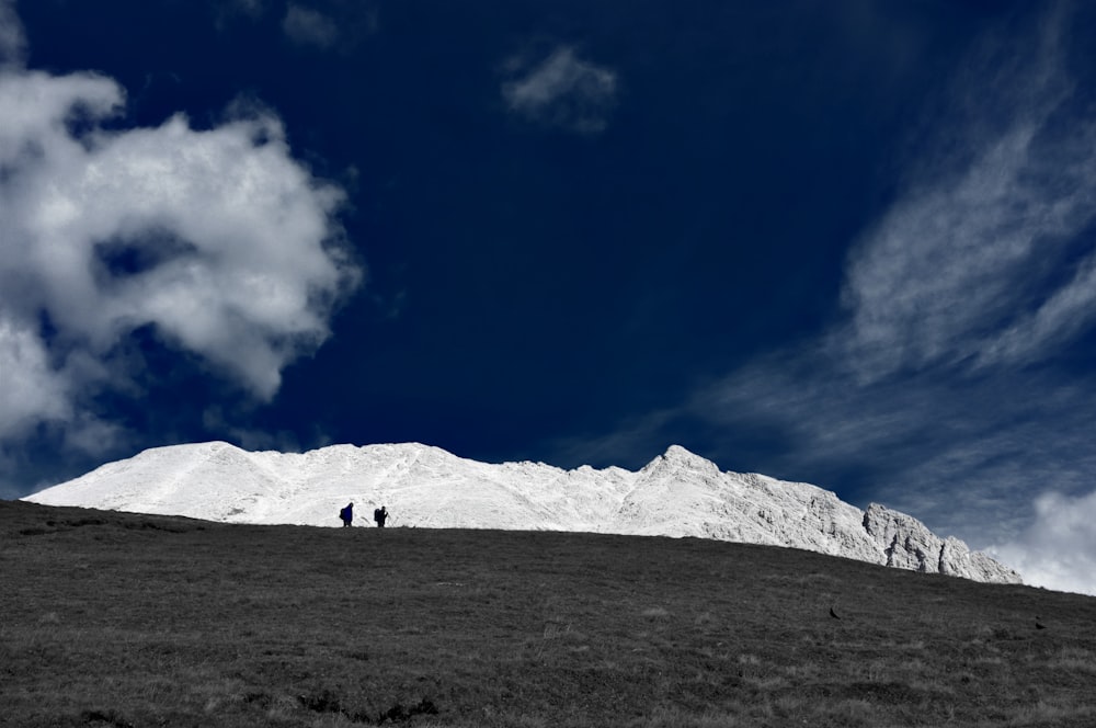 two people walking on hill near mountain under blue and white sky
