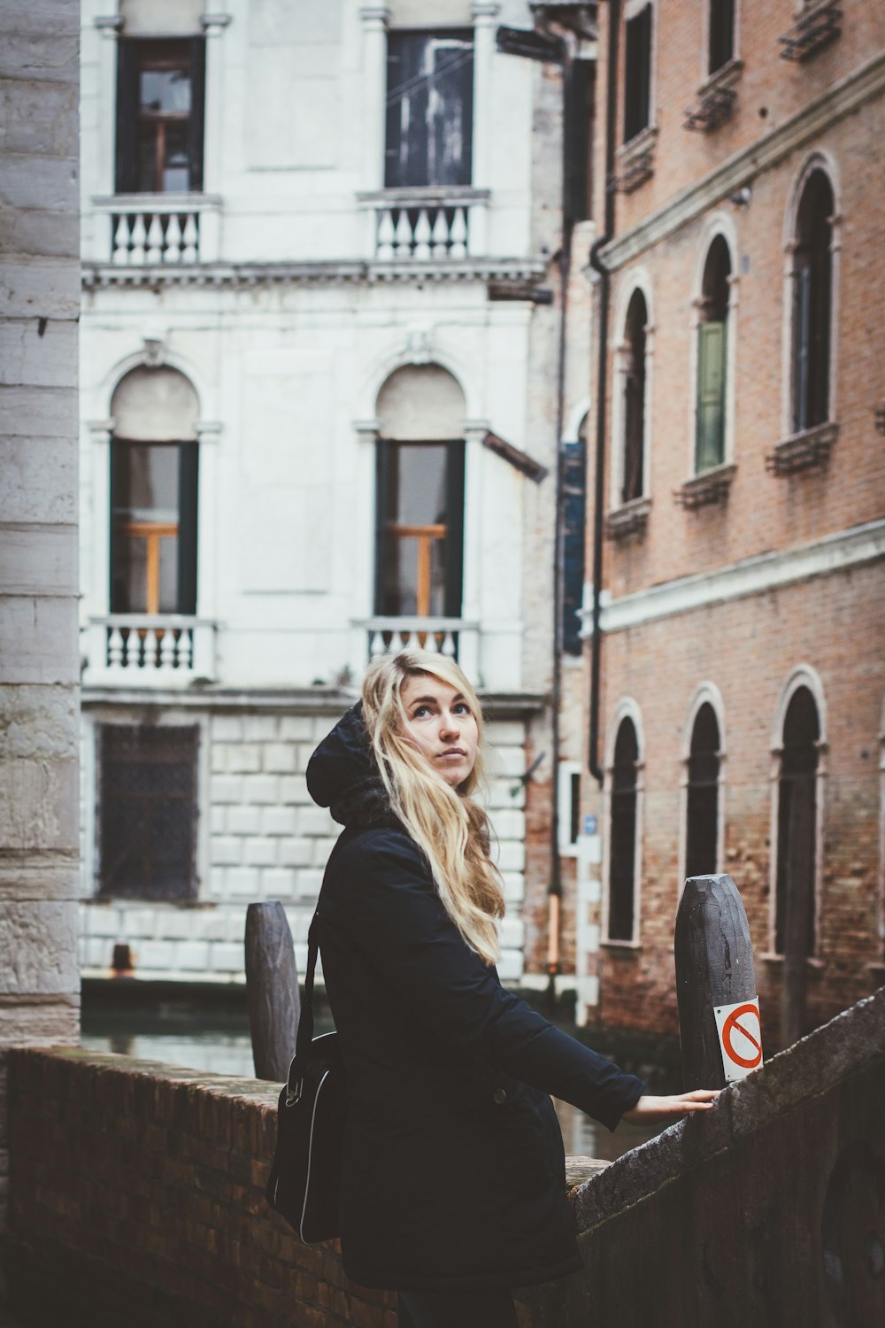 blonde-haired woman in black coat holding on concrete handrail