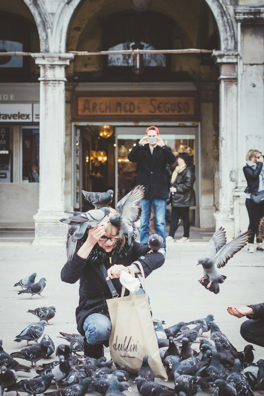 woman kneeling surrounded by flock of pigeons