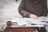 A person wearing a dark jacket is sitting at a table reading a newspaper. The table has various items including an open paint can, brushes, and other art tools. The environment appears to be outdoor on a paved surface.