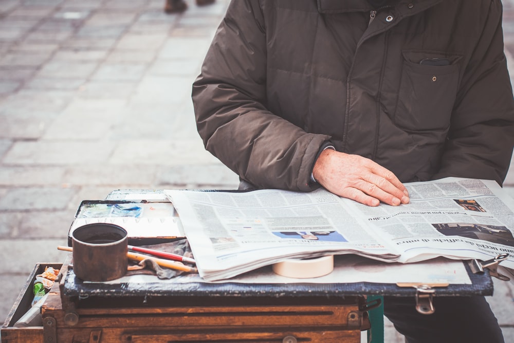 person wearing gray jacket reading newspaper