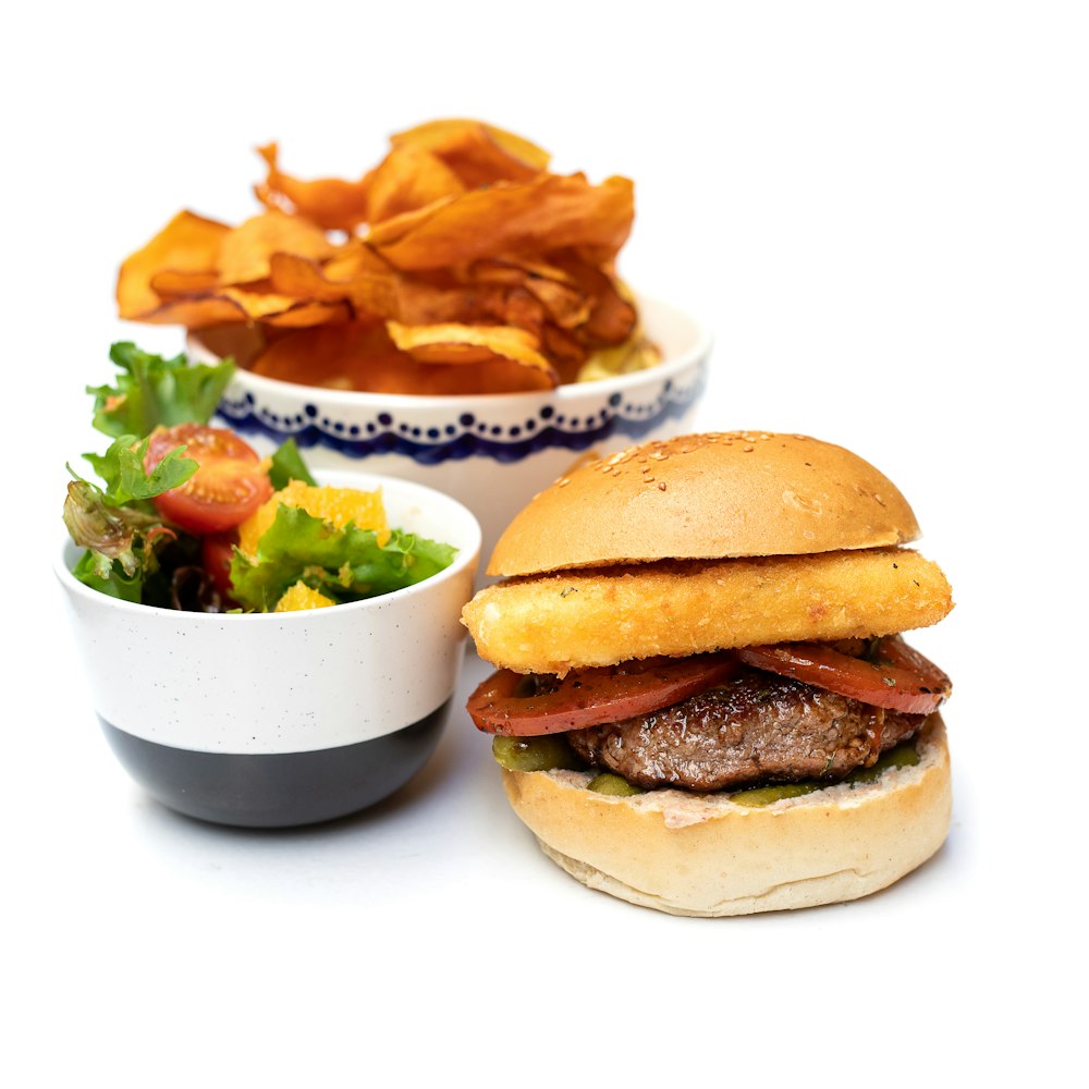 hamburger beside bowl of salad and potato chips