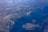 Aerial view of a coastal city with a distinct canal system, surrounded by extensive land and sea areas. The landscape shows a combination of urban structures, agricultural fields, and waterways, with a large airport visible near the center.