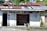 A small, rustic tourist information center with corrugated metal roofing and weathered wooden walls. Shelves filled with books are visible through the open front. A man is sitting in a chair outside, appearing relaxed. The words 'Tourist Information' and 'Books' are painted in blue on the building.