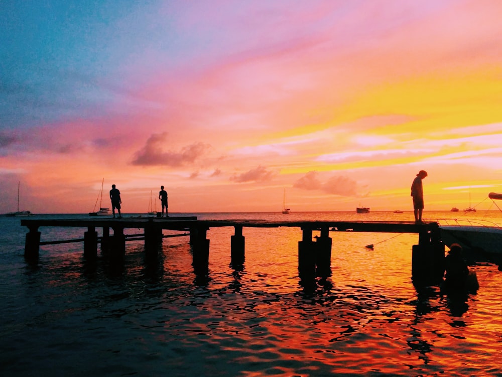 three people on boardwalk at the sea during sunset