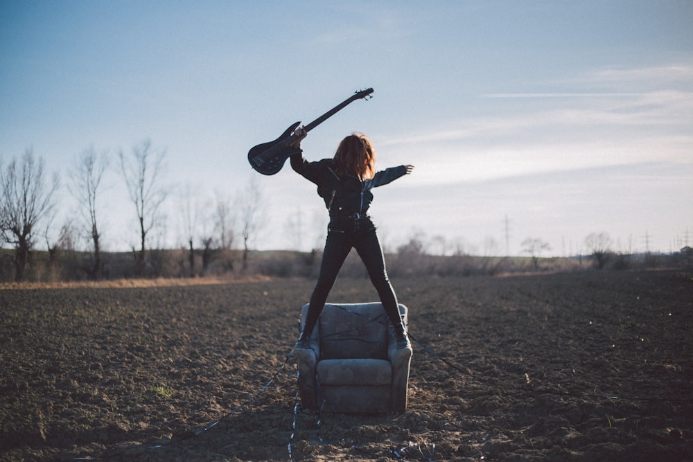 woman standing on sofa chair holding guitar