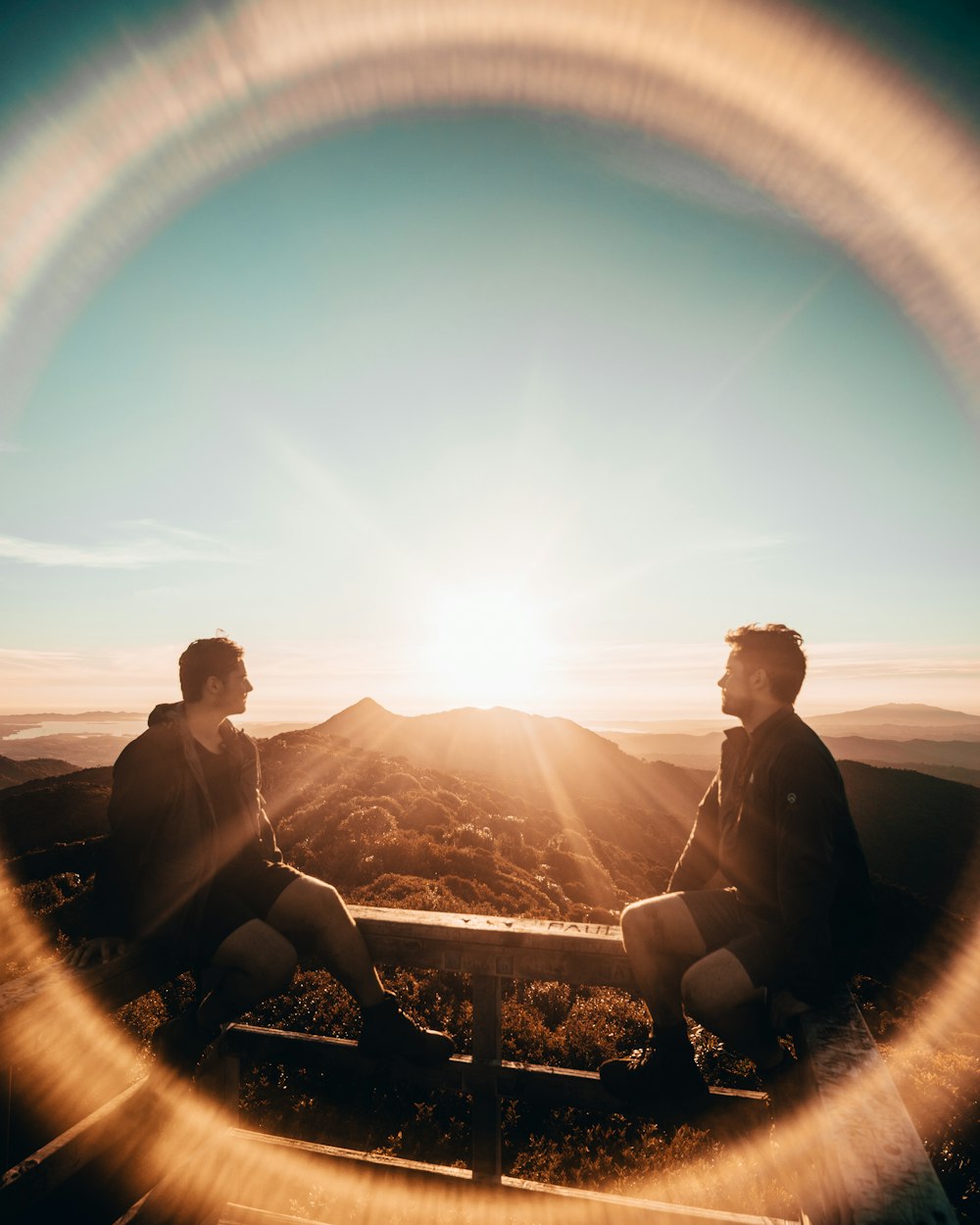 dois homens sentados em cerca de metal durante o nascer do sol