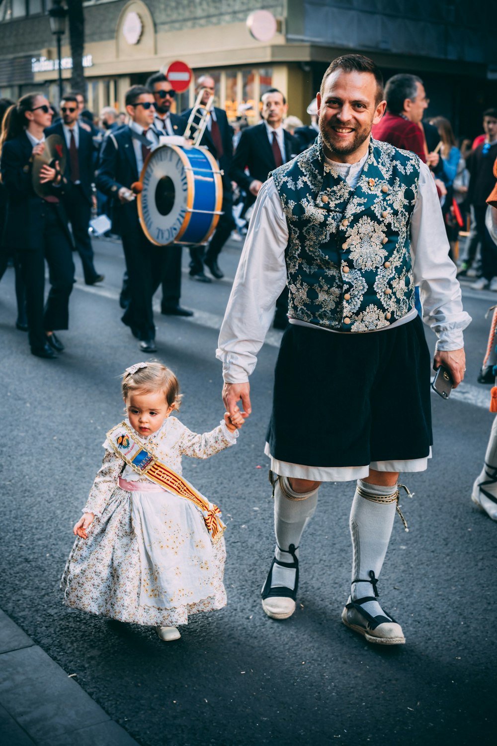 man and girl walks on road with musical parade