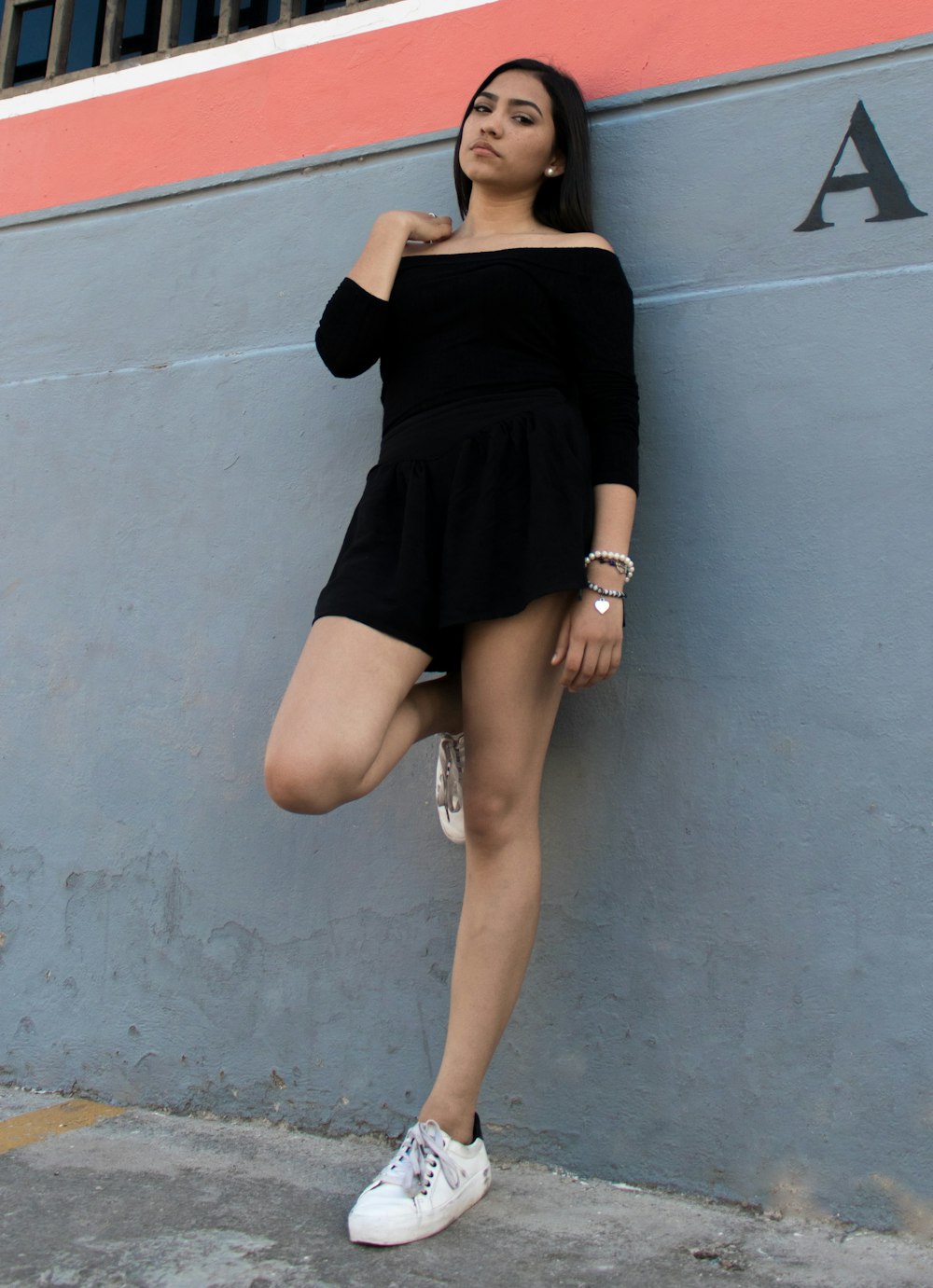 woman wearing black rompers leaning on gray wall