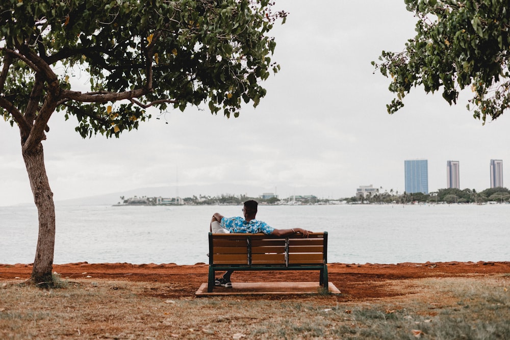 Mann sitzt tagsüber auf einer Bank mit Blick auf ruhiges Meer