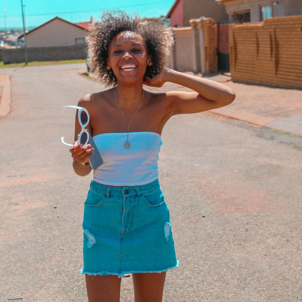 woman standing on road holding sunglasses and iPhone