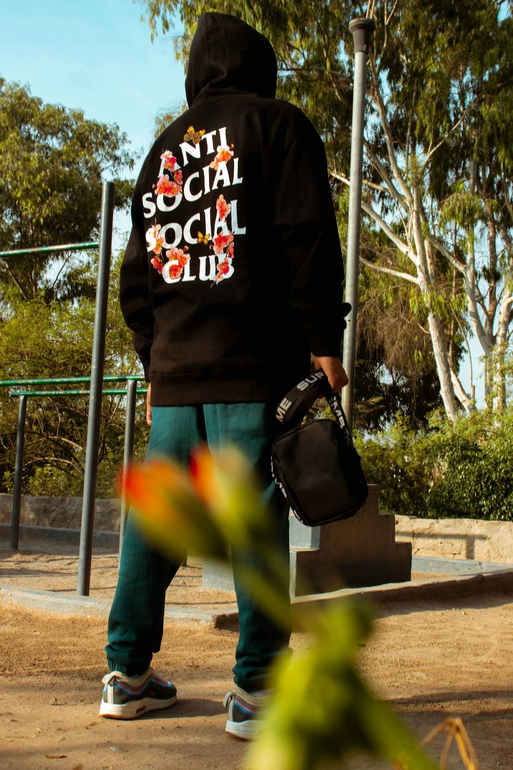 person wearing hoodie standing near street post and trees