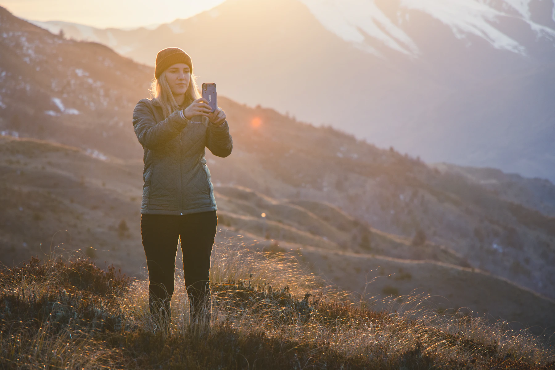 Traveller checking her smartphone on a grassy hillside in warm golden-hour light
