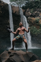 topless man screaming on top of rocks on waterfalls