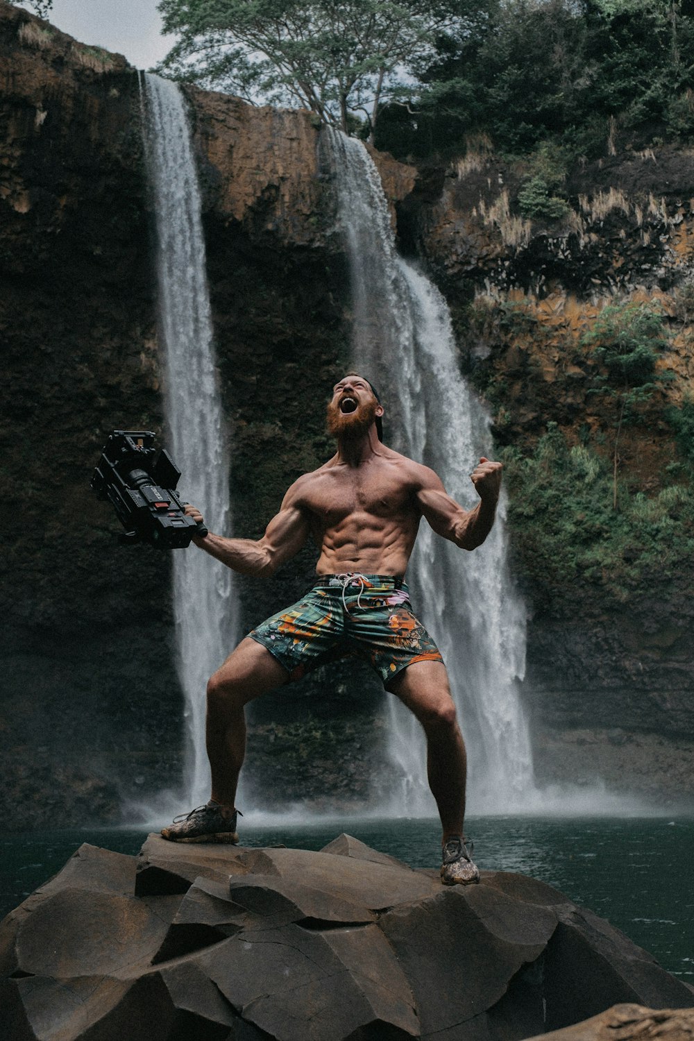 Oben-ohne-Mann schreit auf Felsen an Wasserfällen