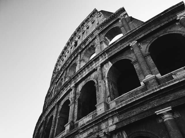 A dramatic black-and-white capture of the Colosseum, showcasing its iconic arches and intricate stonework from a low angle, emphasizing its grandeur and historical significance.