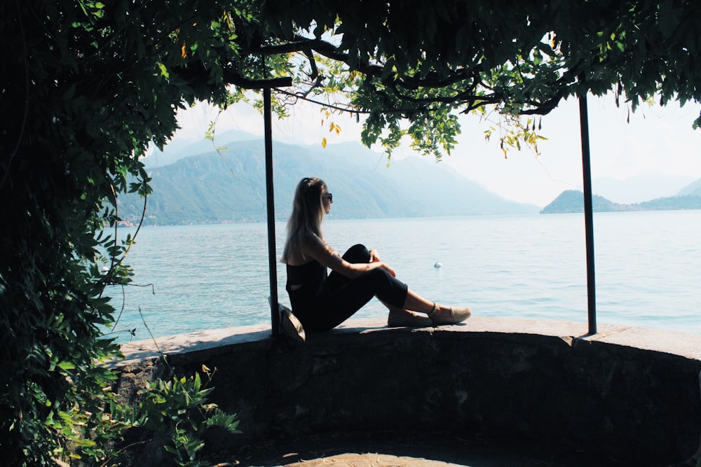 woman sitting on balustrade near body of water