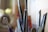 Various art supplies, including paintbrushes and other tools, are placed in a container. The focus is on the tip of a white brush, with other tools out of focus in the background.
