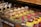 A display of assorted pastries and desserts including eclairs, layered cakes, fruit tarts, and small cakes topped with strawberries, chocolate, and cream. The pastries are arranged on a wooden counter, showcasing a variety of textures and shapes, with a focus on vibrant toppings such as pistachios and berries.