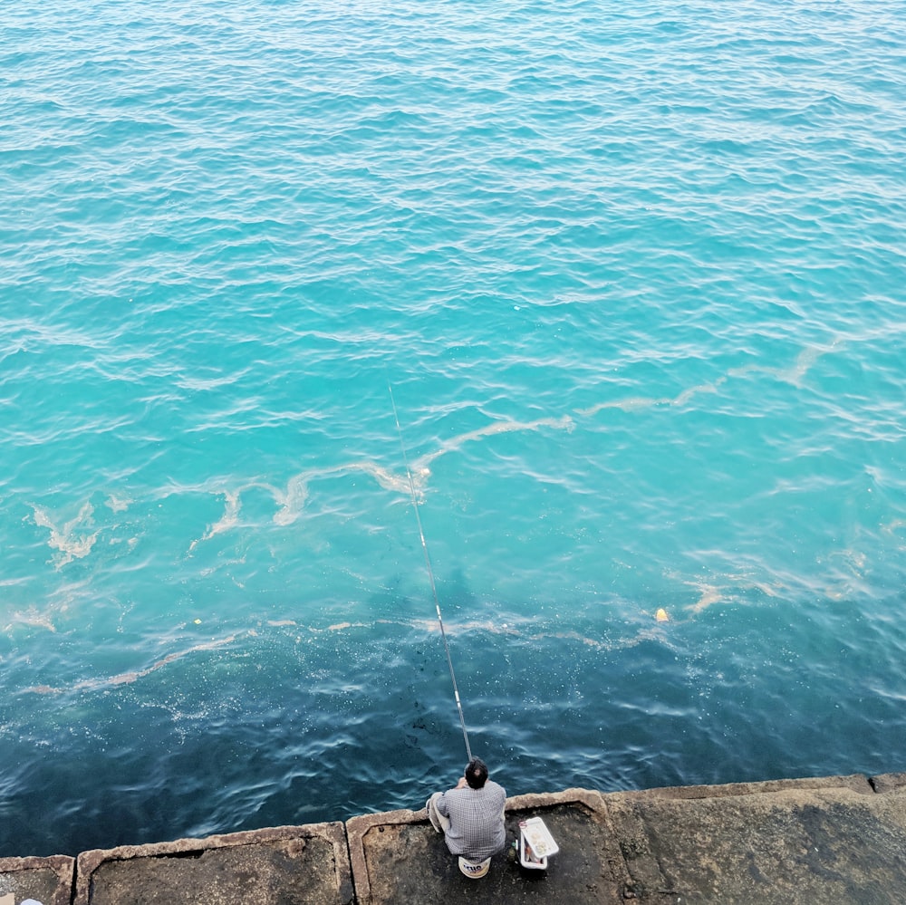 uomo che pesca mentre è seduto su terreno di cemento