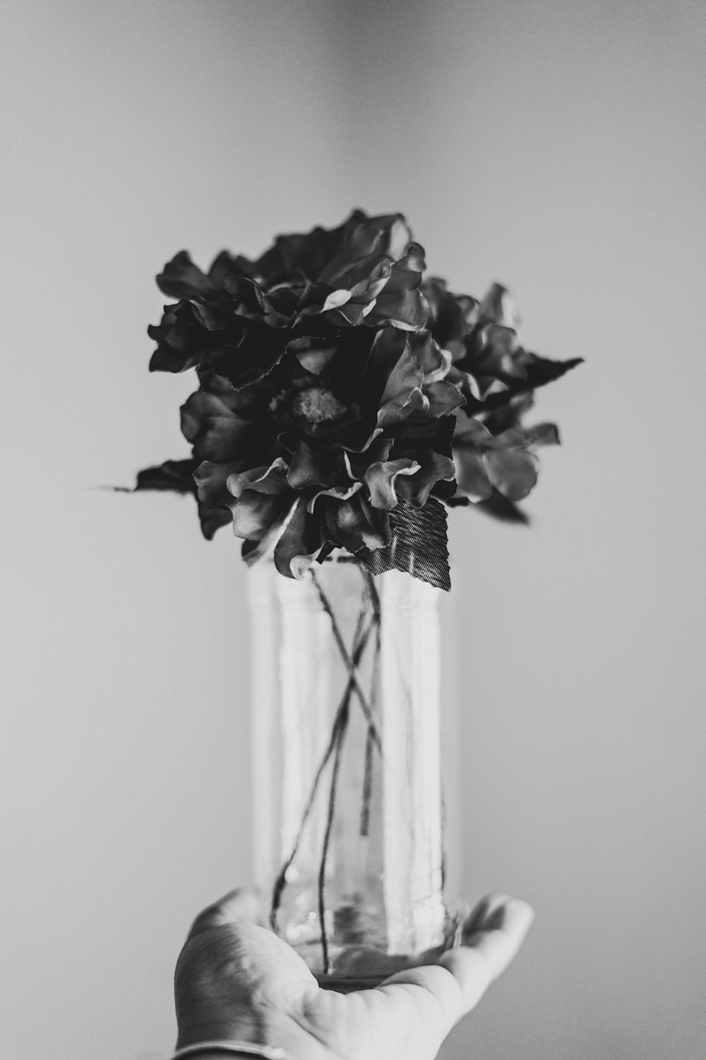 grayscale photography of person holding flower with glass vase