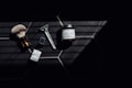 A set of grooming tools and products including a shaving brush, a razor, a bottle of healing post shave spray, and a jar of ultra lather shaving cream arranged on a dark tiled surface with a pattern of hexagonal tiles. The image features dramatic lighting with deep shadows.