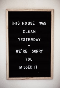 A framed black letter board with white letters spelling out a humorous message about the house being clean yesterday. The sign is simple with plastic letters arranged in a casual style.